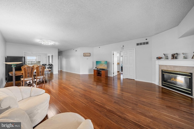 living room featuring a textured ceiling, visible vents, wood finished floors, a tile fireplace, and baseboards