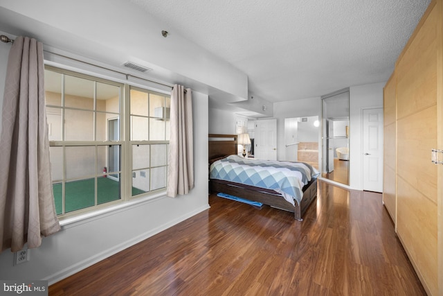 bedroom with visible vents, baseboards, a textured ceiling, and wood finished floors
