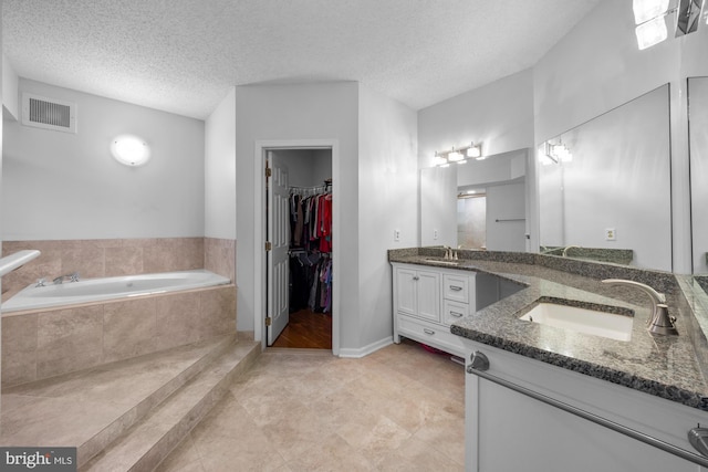 full bath with visible vents, two vanities, a sink, and a garden tub