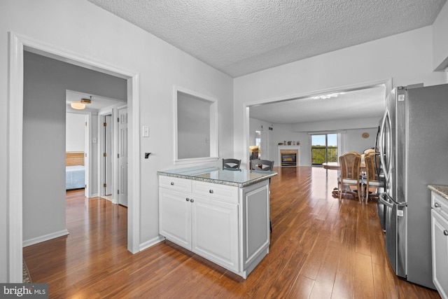 kitchen with white cabinets, a textured ceiling, a glass covered fireplace, freestanding refrigerator, and dark wood-type flooring