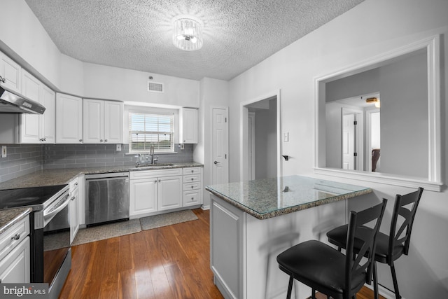 kitchen with dark wood-style flooring, appliances with stainless steel finishes, a breakfast bar area, and white cabinets