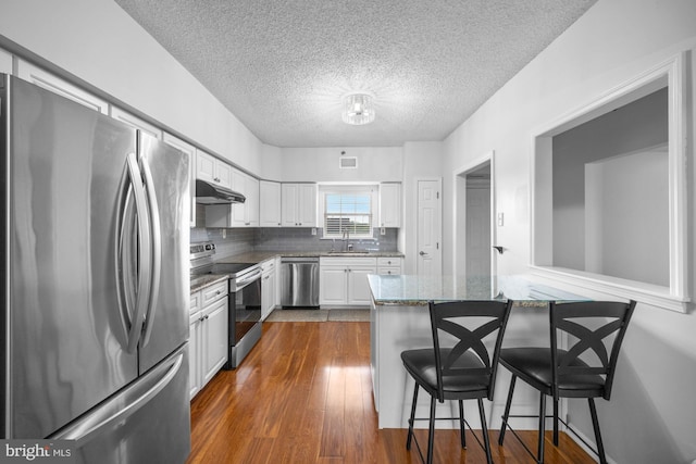 kitchen featuring appliances with stainless steel finishes, a sink, white cabinetry, a kitchen bar, and under cabinet range hood