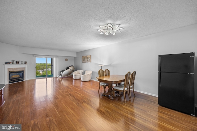 dining area with a glass covered fireplace, a textured ceiling, baseboards, and wood finished floors