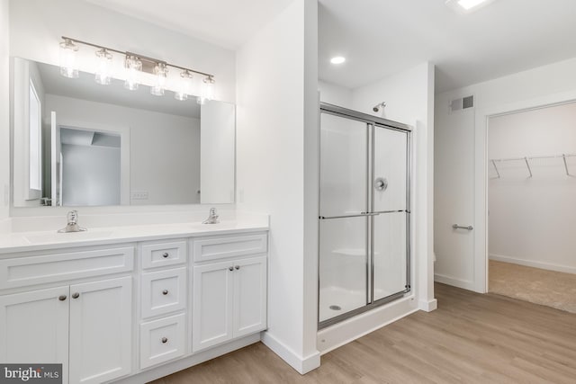 full bathroom featuring visible vents, double vanity, wood finished floors, a sink, and a stall shower