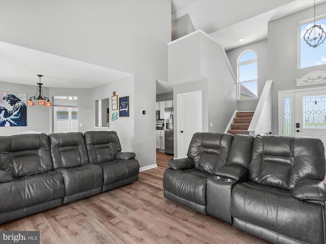 living area with stairs, wood finished floors, baseboards, a high ceiling, and a notable chandelier