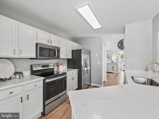 kitchen featuring light stone countertops, appliances with stainless steel finishes, a sink, light wood finished floors, and white cabinetry