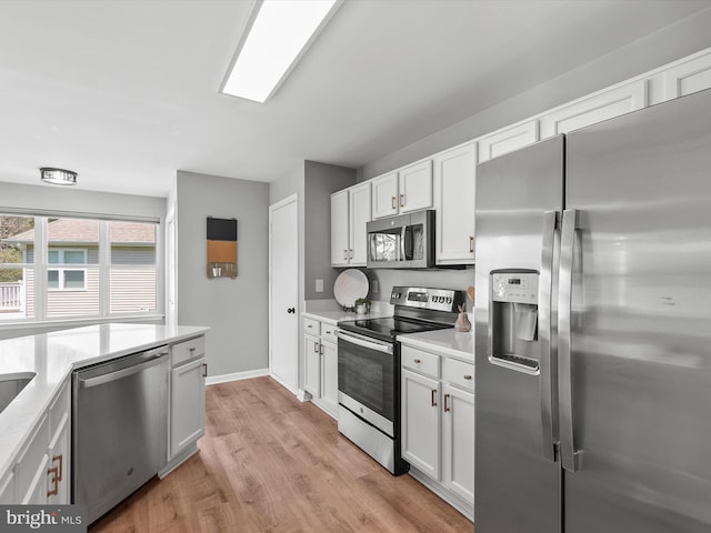 kitchen featuring light countertops, stainless steel appliances, light wood finished floors, and white cabinetry