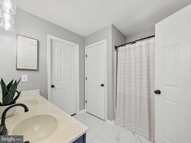 full bathroom with double vanity, marble finish floor, baseboards, a shower with curtain, and a sink