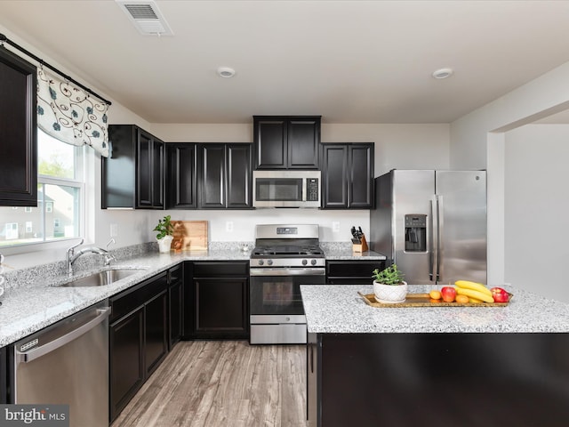 kitchen featuring visible vents, light wood-style floors, dark cabinets, a sink, and appliances with stainless steel finishes