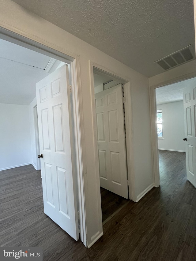 hallway featuring baseboards, dark wood-type flooring, a textured ceiling, and visible vents