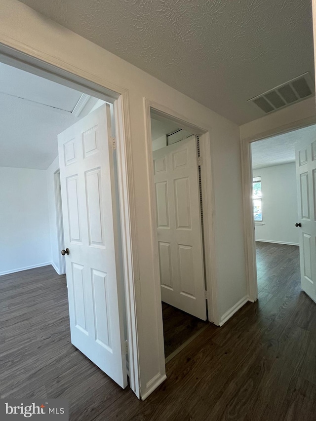 corridor with visible vents, a textured ceiling, dark wood finished floors, and baseboards