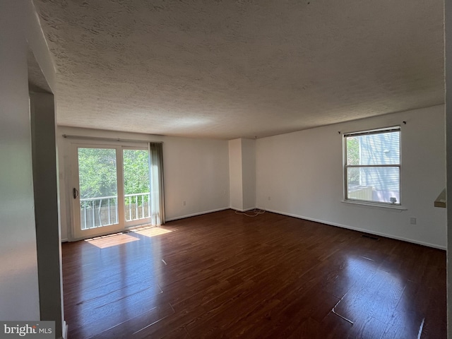 empty room featuring dark wood-type flooring, a textured ceiling, and a wealth of natural light