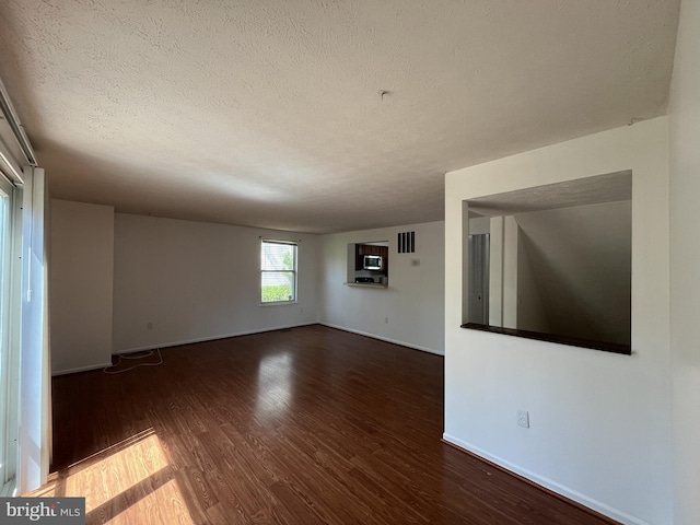 spare room featuring a textured ceiling, baseboards, wood finished floors, and visible vents