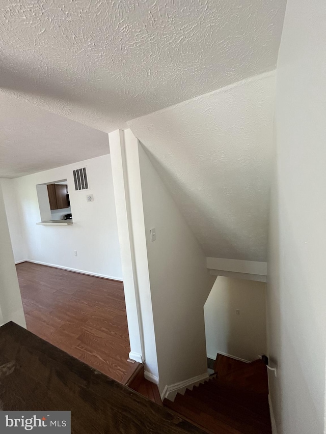staircase featuring visible vents, lofted ceiling, wood finished floors, baseboards, and a textured ceiling