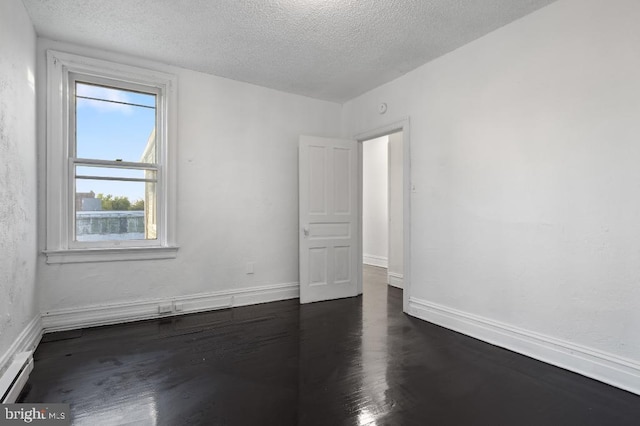 unfurnished room with a textured ceiling, a baseboard heating unit, baseboards, and dark wood-type flooring