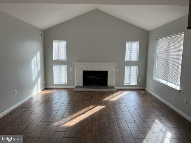 unfurnished living room featuring wood tiled floor, baseboards, a brick fireplace, and lofted ceiling
