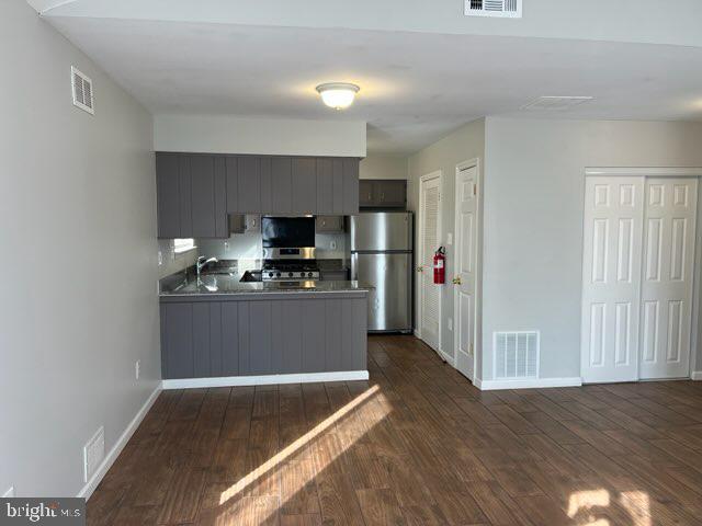 kitchen featuring freestanding refrigerator, a peninsula, visible vents, and dark wood finished floors