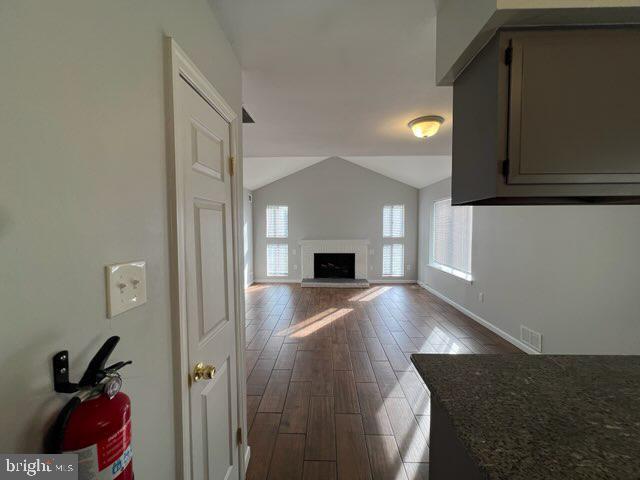 living area with visible vents, baseboards, dark wood-style floors, a fireplace with raised hearth, and vaulted ceiling
