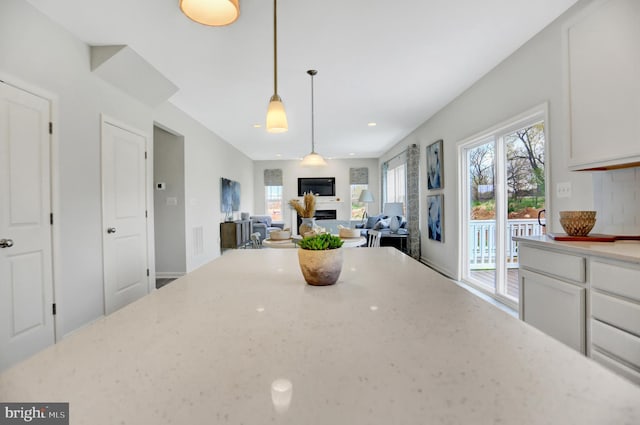 kitchen with pendant lighting, a fireplace, light stone countertops, white cabinets, and recessed lighting