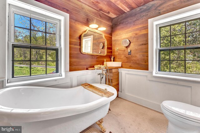 bathroom with a freestanding tub, wood walls, and toilet
