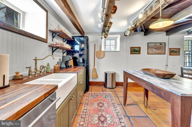 interior space with beam ceiling, a sink, dishwasher, wooden counters, and light tile patterned floors
