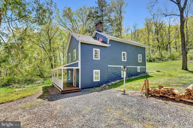 exterior space with a lawn, roof with shingles, a wooded view, and a chimney