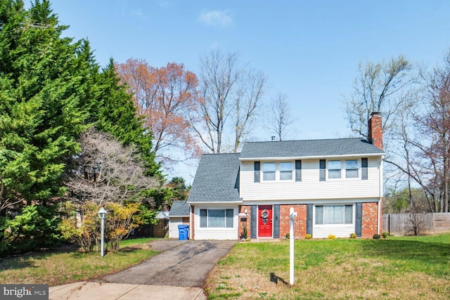 colonial-style house with fence, brick siding, a front yard, a chimney, and driveway