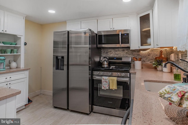 kitchen with appliances with stainless steel finishes, tasteful backsplash, a sink, light stone counters, and white cabinets