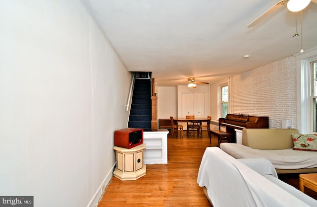 living room featuring light wood-style floors, baseboards, ceiling fan, and stairs