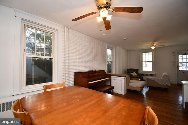 interior space with a ceiling fan, brick wall, a wealth of natural light, and wood finished floors