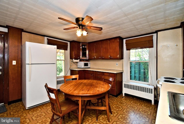 kitchen featuring plenty of natural light, a ceiling fan, radiator, and white appliances