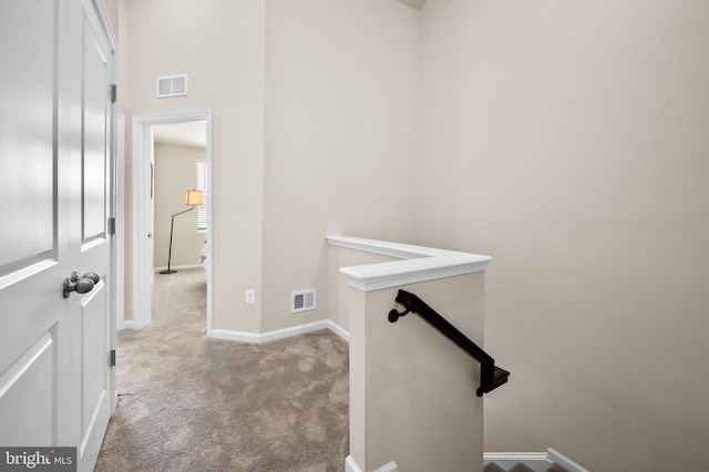 interior space featuring carpet flooring, baseboards, visible vents, and an upstairs landing