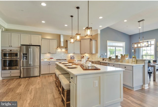 17905 Queen Anne Rd, Upper Marlboro, MD 20774 - kitchen featuring a peninsula, a breakfast bar, wall chimney range hood, light wood finished floors, and appliances with stainless steel finishes