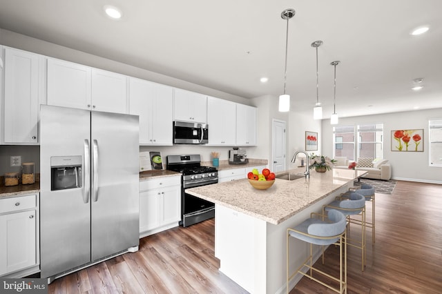kitchen with appliances with stainless steel finishes, a sink, white cabinetry, open floor plan, and wood finished floors