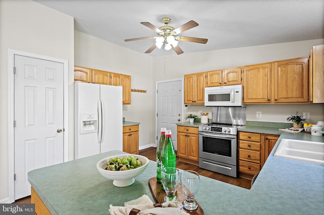kitchen featuring dark wood-style flooring, a sink, white appliances, a ceiling fan, and baseboards