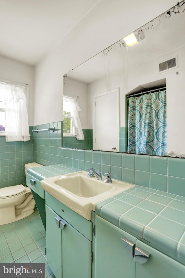 full bath featuring vanity, toilet, tile patterned floors, tile walls, and visible vents
