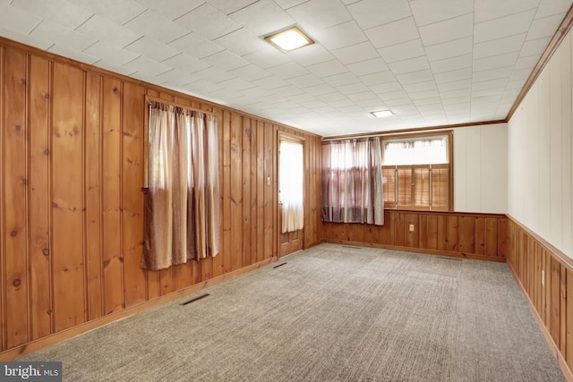 empty room featuring wooden walls, carpet flooring, and visible vents
