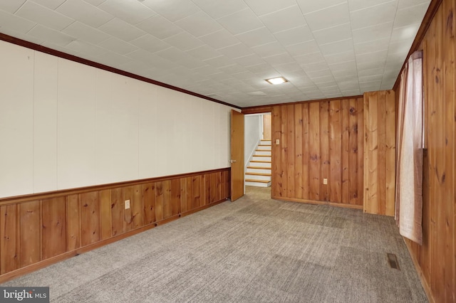 spare room with crown molding, carpet, stairs, and wood walls