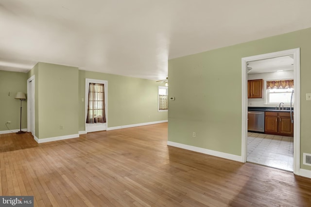 unfurnished living room with visible vents, a ceiling fan, baseboards, a sink, and light wood finished floors