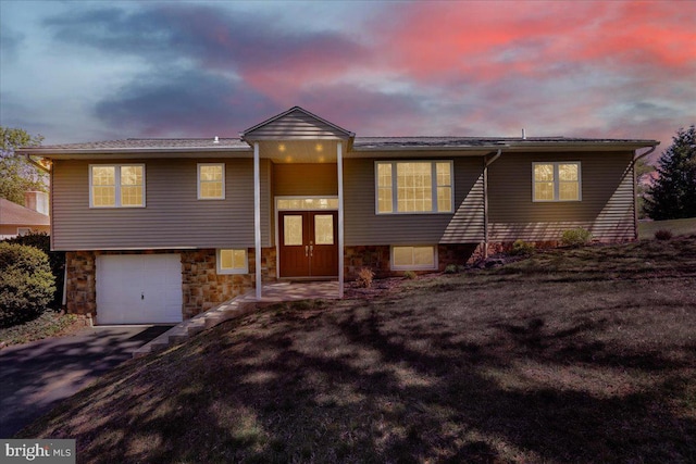 split foyer home featuring an attached garage, driveway, and stone siding