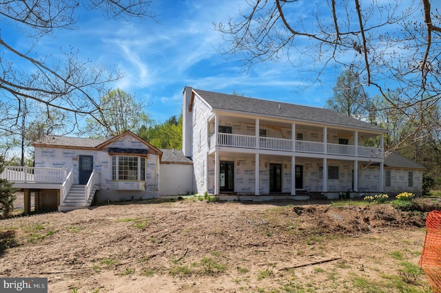 back of house with covered porch, a balcony, and stone siding