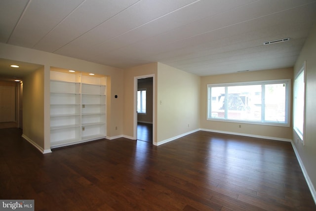empty room featuring baseboards, visible vents, built in features, and dark wood finished floors