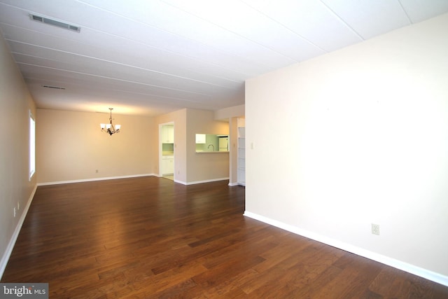 unfurnished room with baseboards, dark wood-type flooring, a chandelier, and visible vents