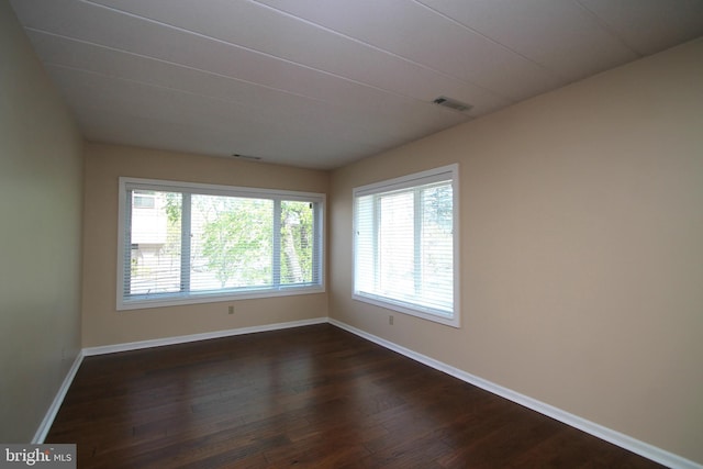 empty room featuring baseboards, dark wood-style flooring, and visible vents