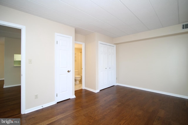 unfurnished bedroom featuring ensuite bath, dark wood finished floors, baseboards, visible vents, and a closet