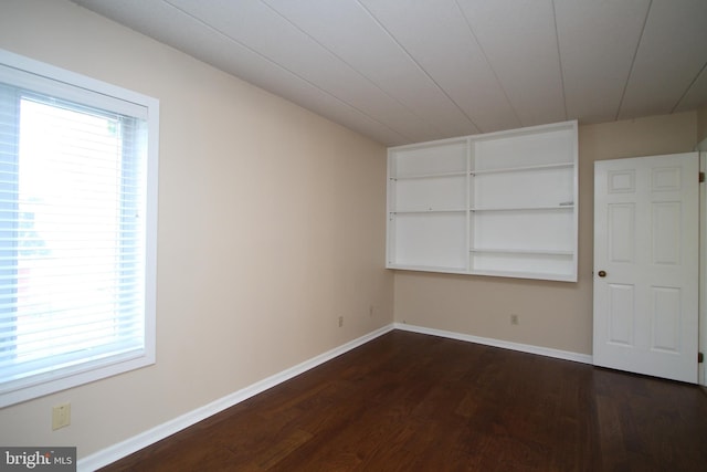 spare room with baseboards, dark wood-style flooring, and built in shelves