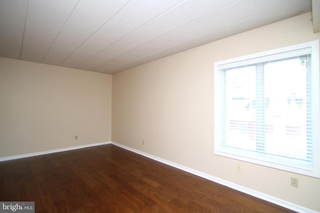 empty room with baseboards, plenty of natural light, and dark wood-type flooring