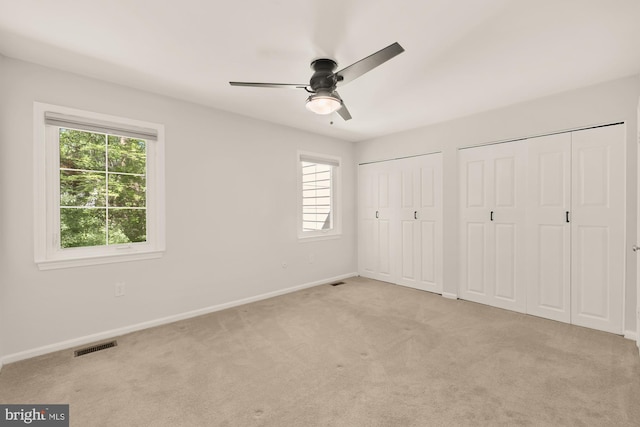 unfurnished bedroom with ceiling fan, visible vents, baseboards, two closets, and light carpet