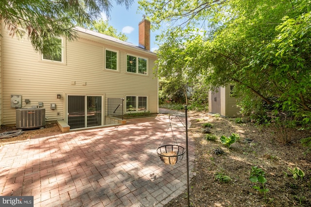 back of house featuring a shed, a chimney, cooling unit, a patio area, and an outdoor structure
