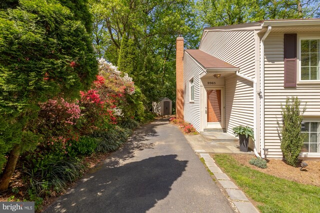 view of side of home featuring an outbuilding, a chimney, driveway, and a shed